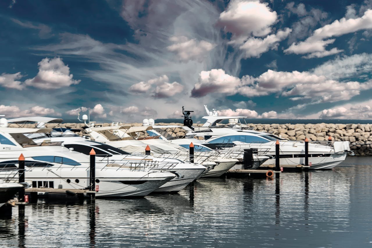 Elegant white yachts docked in a scenic marina with a dramatic cloudy sky and calm waters reflecting the vessels.