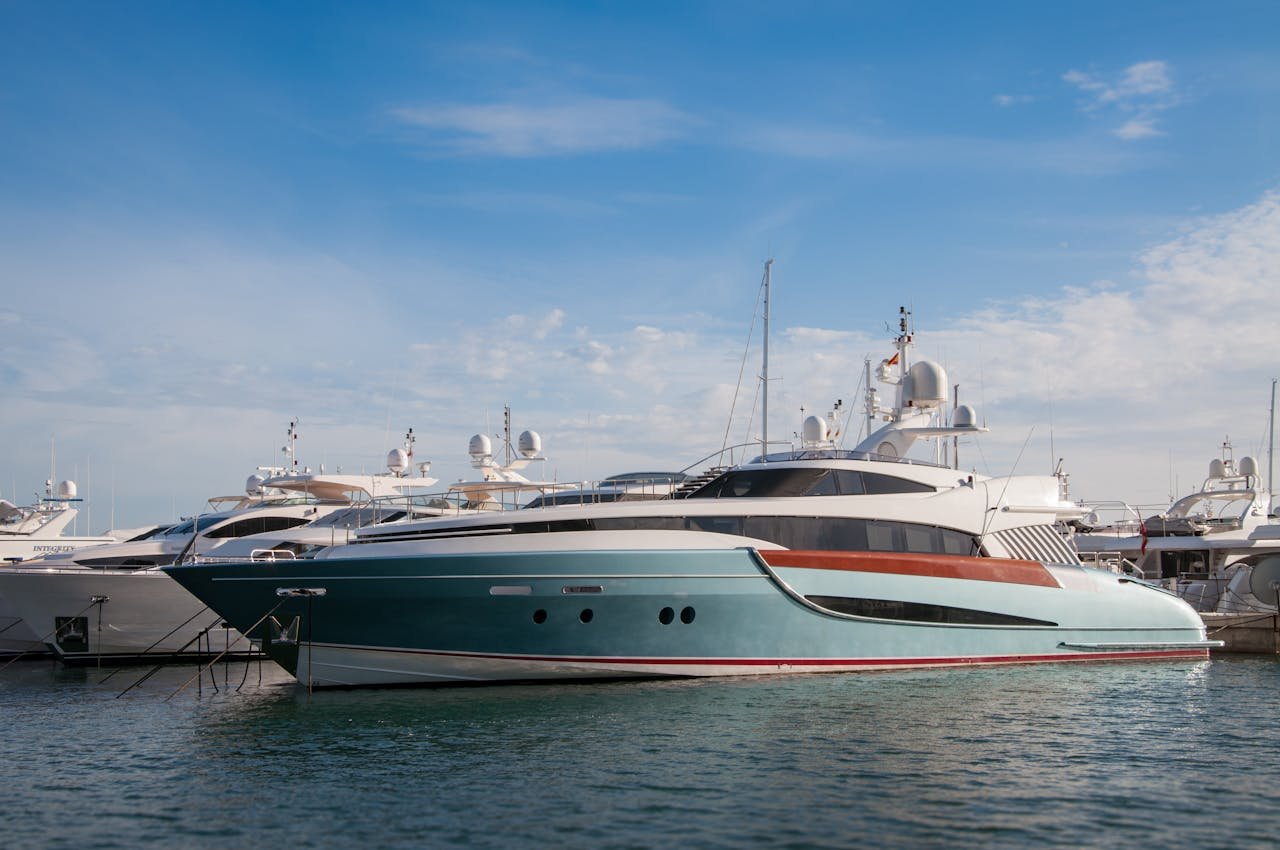 A collection of sleek yachts docked at a serene marina with a bright blue sky above.